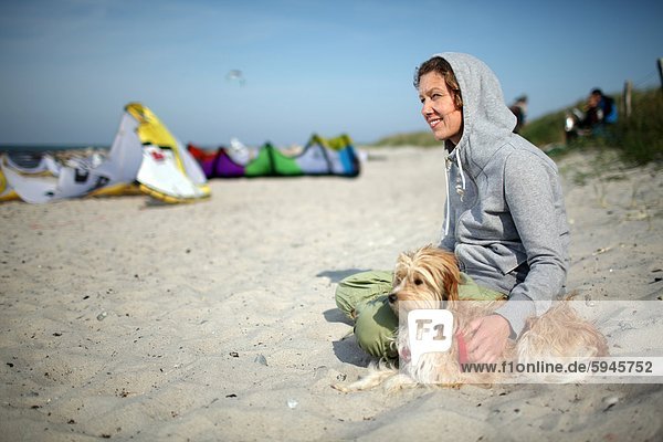 Frau sitzt mit Hund am Strand in Fehmarn  Schleswig-Holstein  Deutschland