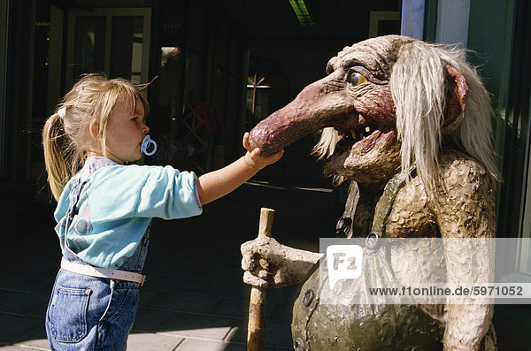 Junges Mädchen mit Dummy in den Mund  berühren Troll Statue mit langer Nase  Norwegen  Skandinavien  Europa