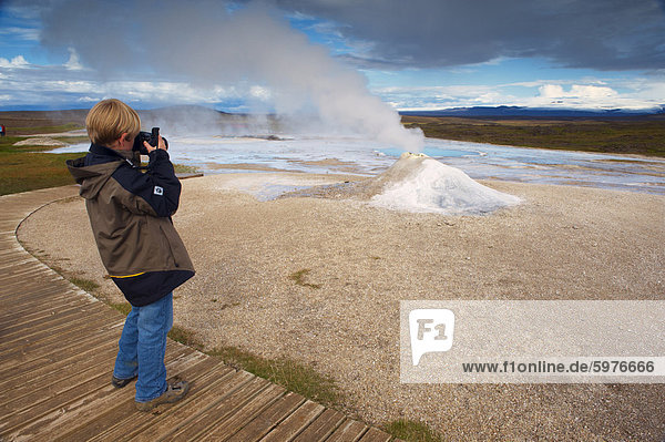 A young boy taking pictures of Oskurholshver (screaming spring)  famous hot spring at Hveravellir  Kjolur  Iceland  Polar Regions