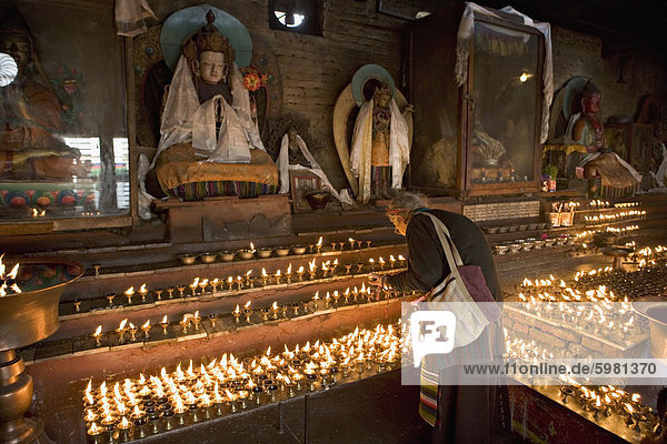 Alte Frau Butter Leuchtlampen vor Buddha-Statuen drapiert mit neuen Seidenschals  in einem kleinen Tempel  an der Boudha oder Bodhnath Stupa  tibetische Neujahr (Lhosar)  Kathmandu  Nepal  Asien