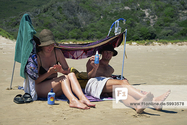 A couple sitting under a beach shade and using skin protection at Wilsons Promontory  Victoria  Australia  Pacific