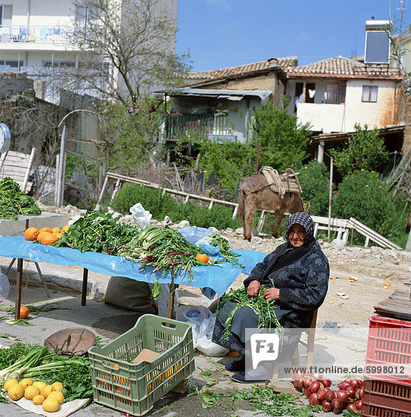 Old woman wearing scarf sitting at a vegetable stall selling greens  lemons and onions  in a village in Greece  Europe
