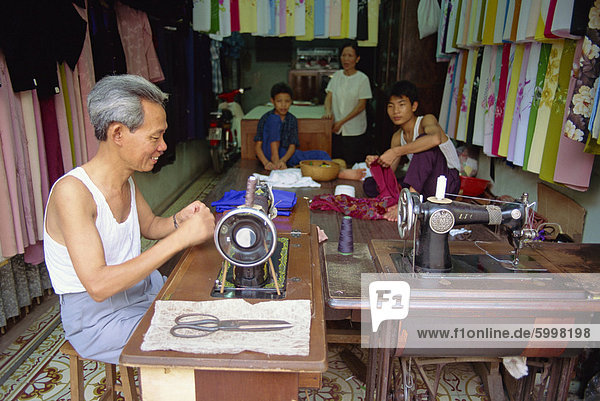 Tailor working at a sewing machine  and his family  in their shop in the old quarter of Hanoi  Vietnam  Indochina  Southeast Asia  Asia