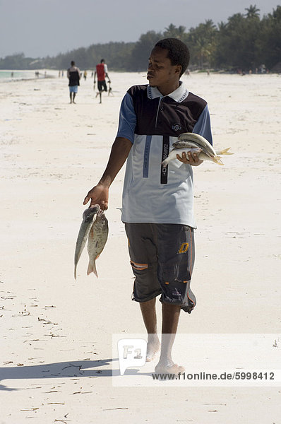 Ein Mann zu Fuß entlang des Strandes mit seinem Fang des Tages  Jambiani  Tansania  Ostafrika  Afrika