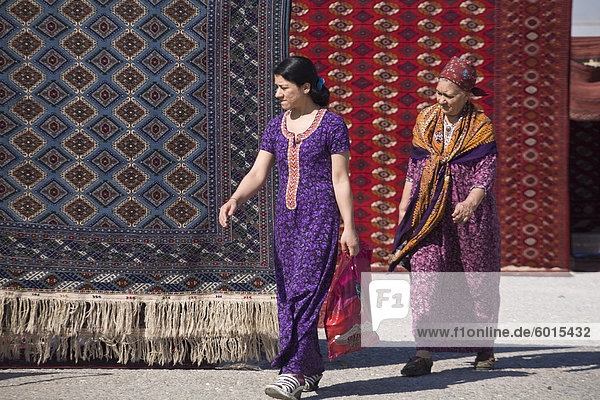 Women walking past carpets  Tolkuchka Bazaar  Turkmenistan  Central Asia  Asia