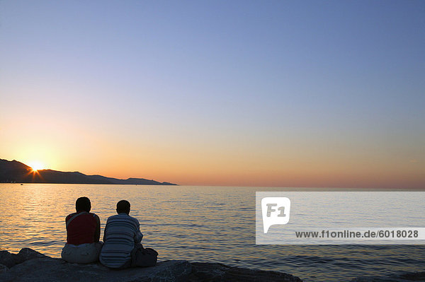 Couple sitting on sea wall watching sunset