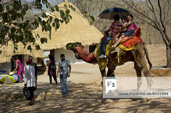 Touristen auf einem Kamel an der Shipgram Handwerker Dorf  Udaipur  Rajasthan  Indien  Asien
