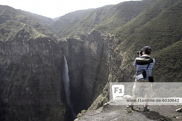 A tourist photographs a waterfall at the Geech Abyss  in the Simien Mountains National Park  Ethiopia  Africa
