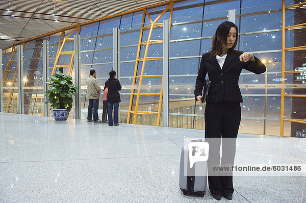 Eine chinesische geschäftsfrau  Blick auf ihre Uhr am Beijing Capital Airport Teil des Terminal 3 Neubau eröffnet Februar 2008  zweitgrößte Gebäude der Welt  Peking  China  Asien