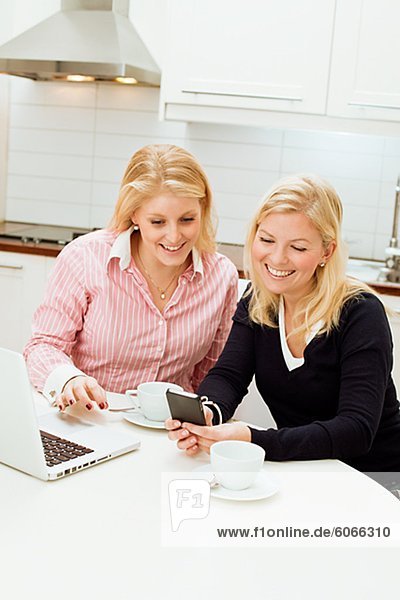 Two young women using laptop in kitchen