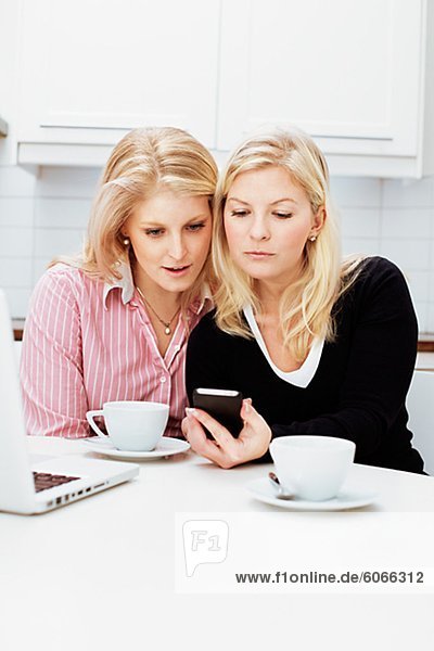Zwei junge Frauen mit Handy in Küche
