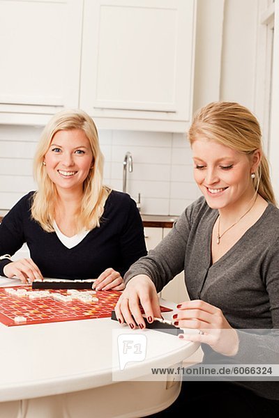 Two young women playing board game in kitchen
