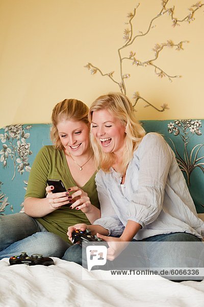 Zwei junge Frauen mit Handy im Schlafzimmer