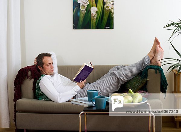 Mitte erwachsener Mann am Sofa liegen und lesen Buch