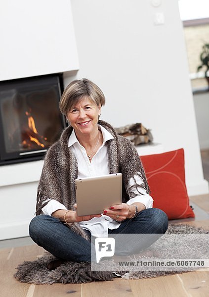 Portrait of mature woman sitting by fire place with digital tablet