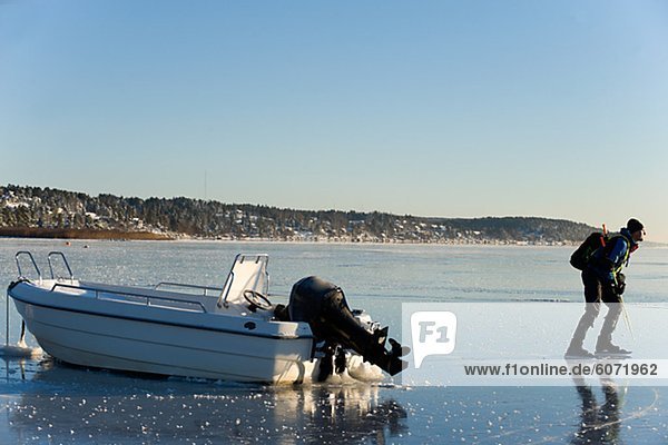Man Eislaufen in Küstennähe mit festgemachten Motorboot
