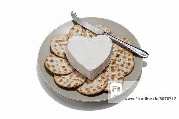 Ein herzförmiges Käse mit Cracker und Käsemesser auf einen Teller