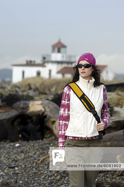 A woman walks on a rocky shore with a lighthouse in the background in Puget Sound.