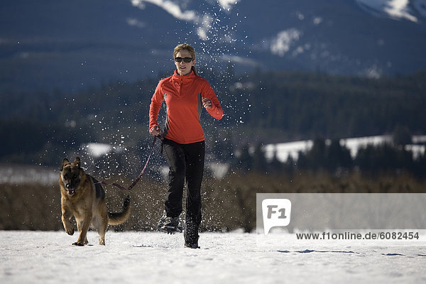 Young woman in snowshoes runs though snow with German shepherd dog near Mt. Hood  Oregon.