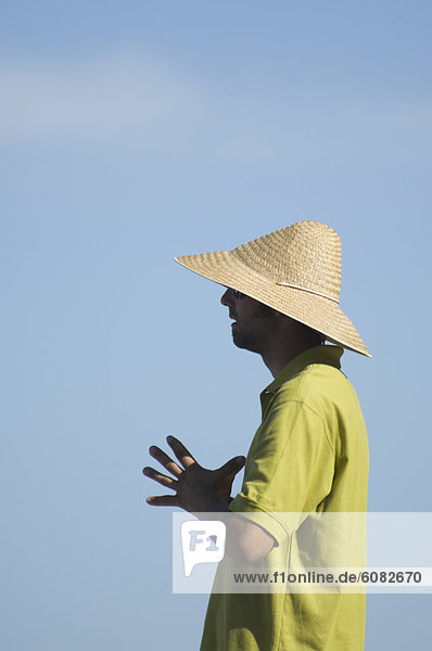A young twenty something sports a straw hat on a sunny day.
