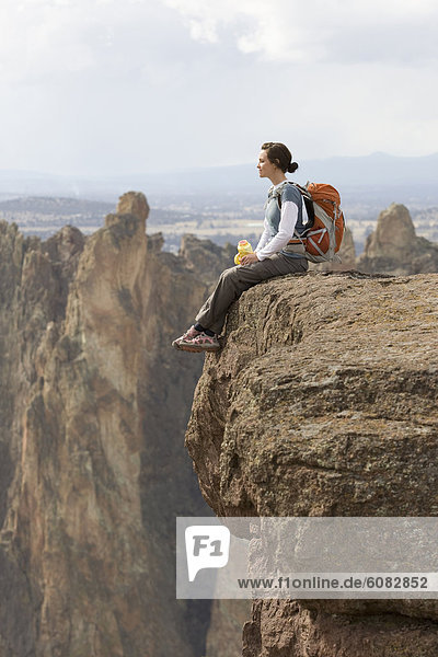 A woman with a day pack and water bottle sits on the edge of a steep cliff.