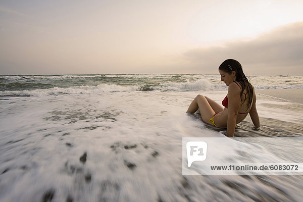 A young woman relaxing at sunset while sitting in the waves on Chiarone Beach in Capalbio  Tuscany  Italy.