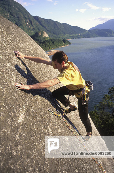 A man rock climbing with water in the background in Squamish  British Columbia  Canada.