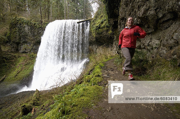 A woman trail running next to a waterfall in Silver Falls State Park  Oregon  USA.
