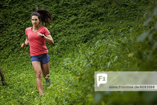 Woman trail running through a green meadow in the woods.