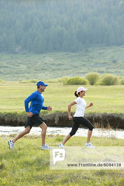 An athletic couple trail running through a field next to a river.