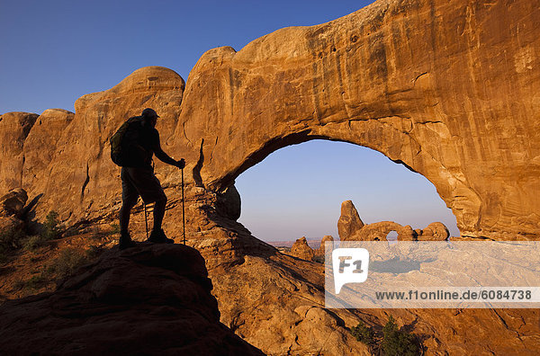 A silhouetted hiker stands looking at an arch in Arches National Park  Utah.
