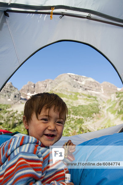 A 14 month boy eats a snack while sitting on a pillow of sleeping bags in a tent at about 11 000 feet in the Maroon Bells in Snowmass Wilderness just outside of Aspen  Colorado.