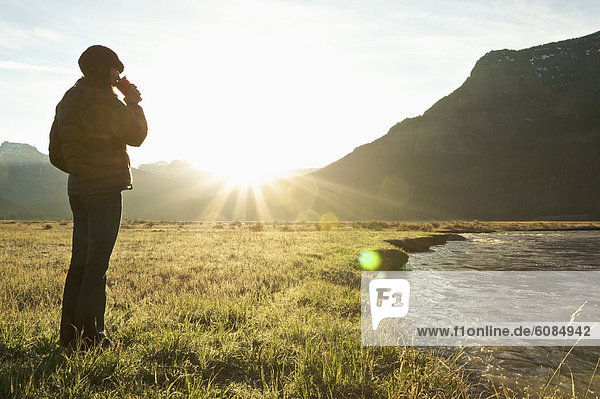 A woman drinks coffee and watches the sunrise from a field in Yellowstone National Park.