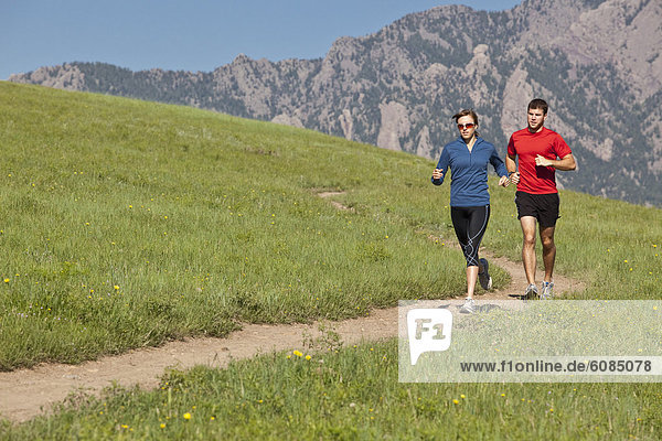 A man and woman run on a grassy trail in the foothills of the Rocky Mountains  Colorado.