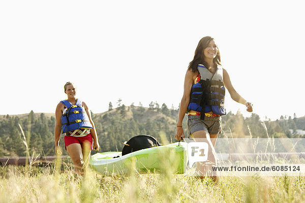 Two girls in life jackets carry a green kayak through a field after a day of kayaking the Yellowstone River in Eastern Montana.