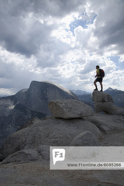 A female hiker on granite boulders on the North Dome at Yosemite National Park  with Half Dome in the background.