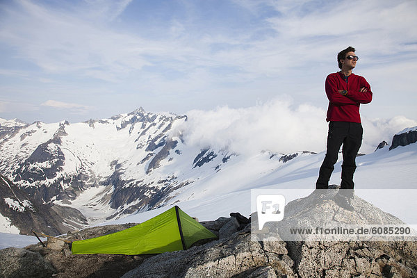 A young climber stands on a rock outcrop near his tent while climbing on a glacier in the mountains.