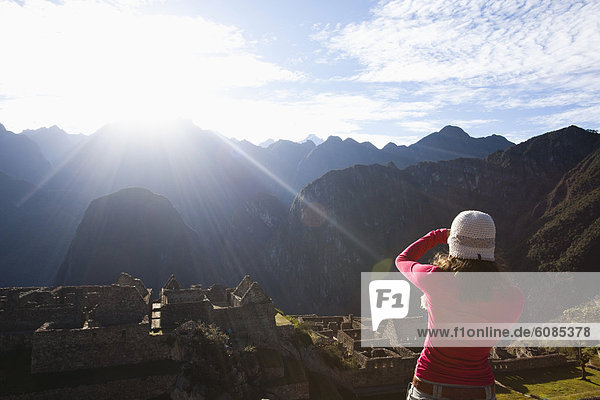 A teenager takes a photograph of the rising sun over a steep valley and the ruins of a lost civilization.