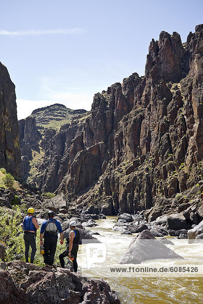 Three men  dressed in river gear with rescue bags  size up the rapids ahead of them  on the Owyhee River.