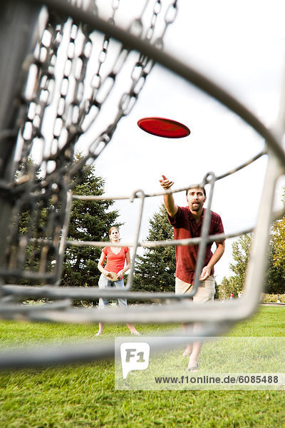 A man and woman play disk golf.