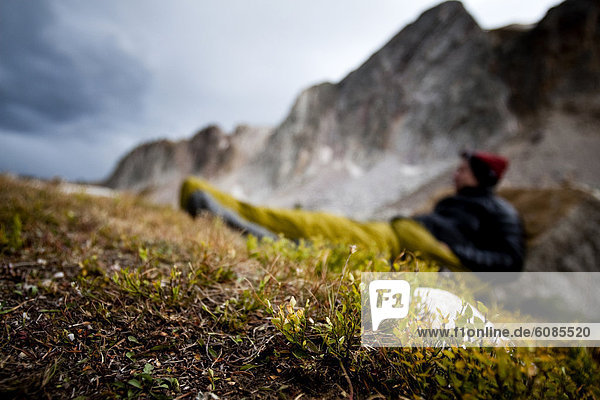 Man bivouacs in alpine meadow with the Snowy Range Mountains in the background.