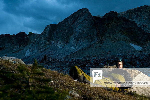 Man bivouacs in alpine meadow with the Snowy Range Mountains in the background.