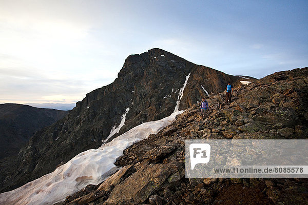 A man and woman hike down from the 14 000 ft peak Mount of Holy Cross  just after sunrise in Colorado.