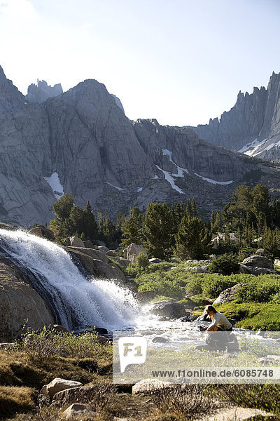 A female hiker fills a water bottle from a stream in the Cirque of the Towers  Wind River Range  Wyoming.