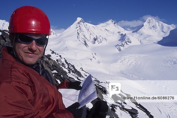 Man high on a snow covered peak with a map and a vast view of winter in Alaska.
