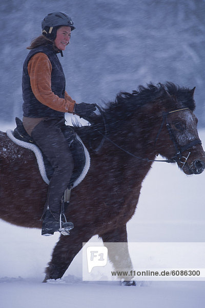 Woman riding a horse in deep snow during a snowstorm.