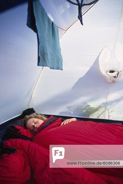 Woman asleep in a sleeping bag in a tent during an extended sea kayak trip in Montana.