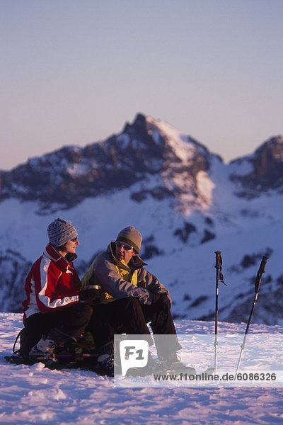 Couple stops to rest while snowshoeing on snowy mountain flanks in Washington.