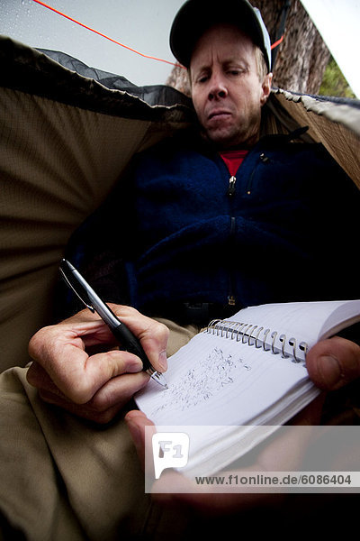 A man takes a short rest to write in a journal in a hammock with a rain fly during rainy weather in the Snowy Range  Wyoming.