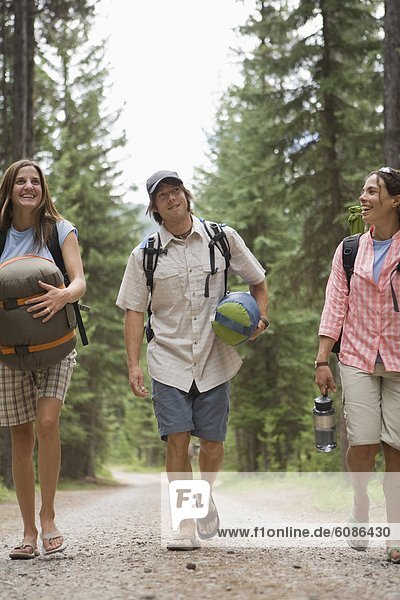 Group of twenty-something adults walking down a dirt road to camp in woods.